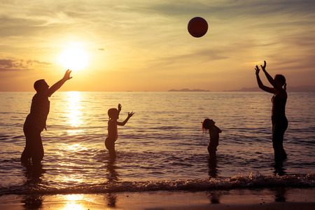 Silhouette of happy family who playing with the ball on the beach at the sunset time. Concept of friendly family.の写真素材