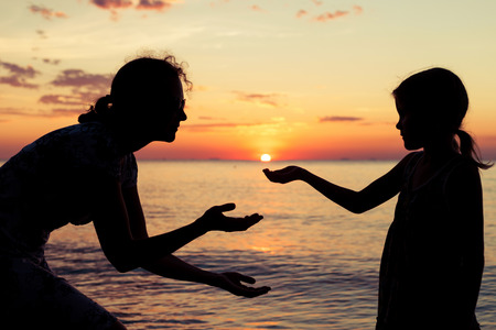 Mother and daughter playing on the beach at the sunset time. Concept of friendly family.の写真素材