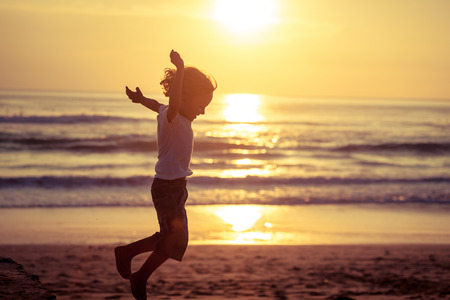 Happy little boy jumping on the beach at the sunset timeの写真素材