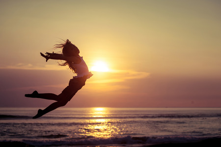 Happy little girl jumping on the beach at the sunset timeの写真素材