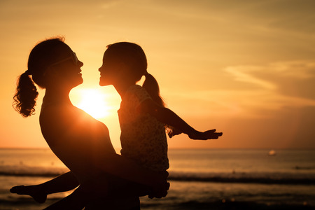 Mother and daughter playing on the beach at the sunset time. Concept of friendly family.の写真素材