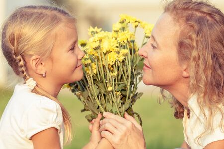 Mother and daughter playing with flowers on the grass at the day time. Concept of friendly family.の写真素材