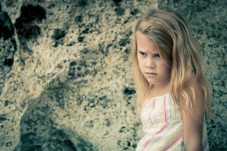 Portrait of sad blond little girl sitting on the beach at the day time