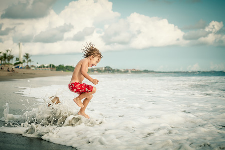 Portrait of little boy jumping on the beach at the day timeの写真素材