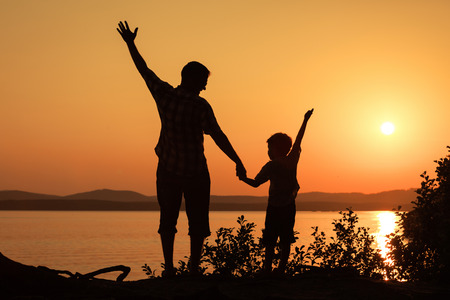 father and son playing on the coast of lake in the mountains of at the sunset timeの写真素材