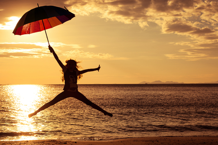 Happy girl with an umbrella jumping on the beach at the sunset timeの写真素材
