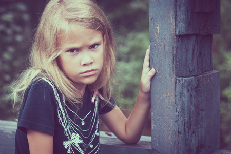Portrait of sad blond little girl sitting on the bridge at the day timeの写真素材