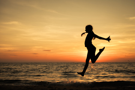 Happy teen girl  jumping on the beach at the sunset timeの写真素材