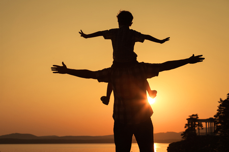 father and son playing on the coast of lake in the mountains of at the sunset timeの写真素材