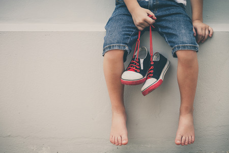 Little boy  sitting near the house and keeping the youth sneakers in his hands of at the day time.の写真素材