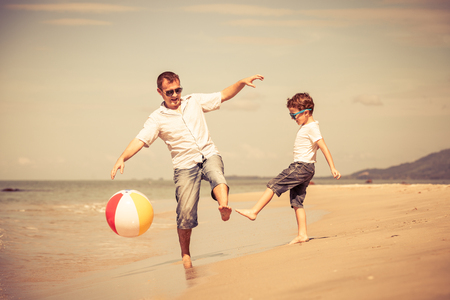 Father and son with ball playing soccer on the beach at the day time. Concept of friendly family.の写真素材