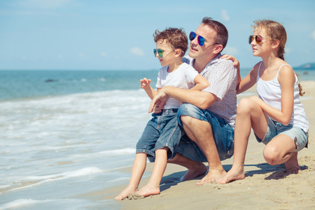 Father and children sitting on the beach at the day time. Concept of happy friendly family.の写真素材