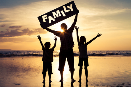 Happy family standing on the beach at the sunset time. Parents hold in the hands  inscription "Family". Concept of happy family.の写真素材