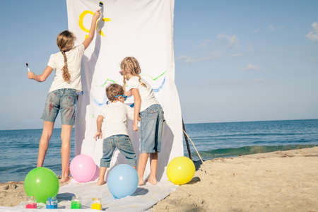 Two sisters and brother playing with paint on the beach at the day time. Concept Brother And Sister Together Foreverの写真素材