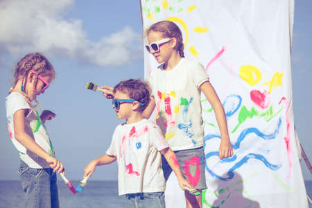 three children playing with paint on the beach at the day time. Concept Brother And Sister Together Foreverの写真素材