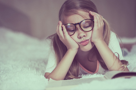 Portrait of sad little girl lying on bed at the day time. Concept of sad childhood.の写真素材