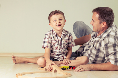 Daddy with little boy playing with toy train on the floor at the day time. Concept of friendly family.の写真素材