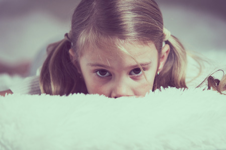 Portrait of sad little girl lying on bed at the day time. Concept of sad childhood.の写真素材