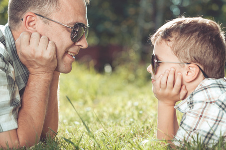 Father and son lying near the tree in the garden at the day time. Family having fun on the nature. Concept of friendly family and of summer vacation.の写真素材