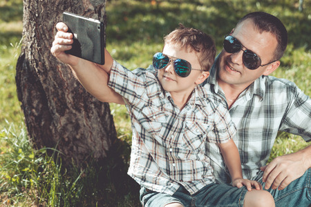 Father and son sitting near the tree in the garden at the day time. Family having fun on the nature. Concept of friendly family and of summer vacation.の写真素材