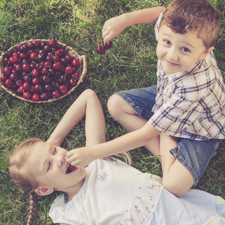 Cute happy little children with basket of cherries lying near the tree in the garden  at the day time. Concept of healthy food.の写真素材