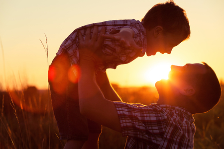 Father and son playing in the park at the sunset time. People having fun on the field. Concept of friendly family and of summer vacation.の写真素材