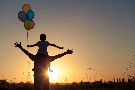 Father and son playing with balloons in the park at the sunset time. People having fun on the field. Concept of friendly family and of summer vacation.の写真素材