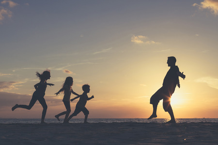 Father and children playing on the beach at the sunset time. People having fun on the sea. Concept of friendly family and of summer vacation.の写真素材
