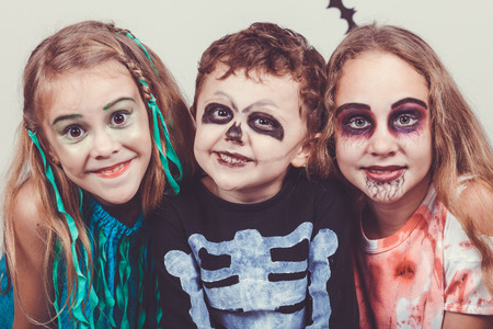 Happy brother and two sisters on Halloween party. People having fun indoor. Children wearing costumes zombies, skeletons and witches. Concept of children ready for a party.の写真素材