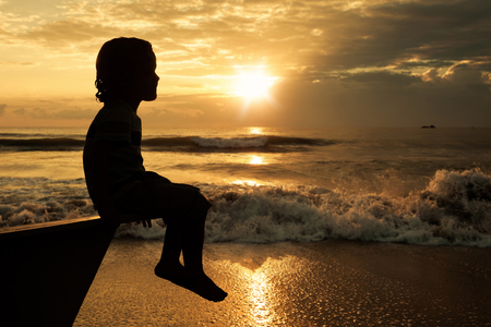 happy little boy sitting on beach at the dawn time. Concept of life.の写真素材