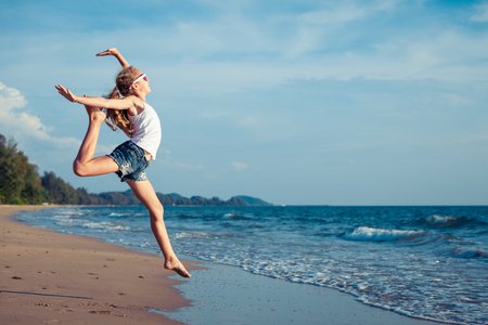 One teen girl  jumping on the beach at the day time.  Teenager having fun outdoors. Concept of happy summer vacation.の写真素材