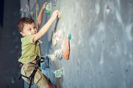 little boy climbing a rock wall indoor. Concept of sport life.の写真素材