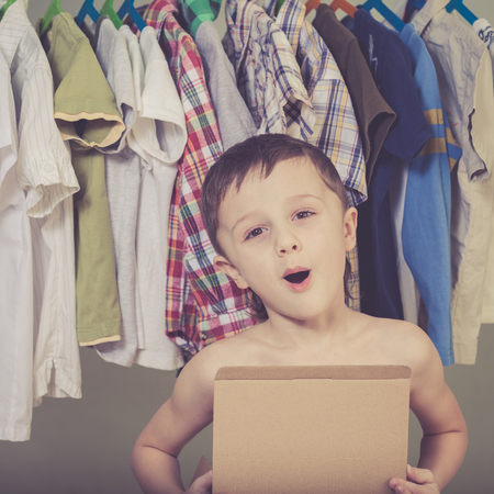 portrait of a little boy standing near a hanger with clothes at home at the day timeの写真素材