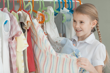 portrait of a little girl standing near a hanger with clothes at home at the day timeの写真素材