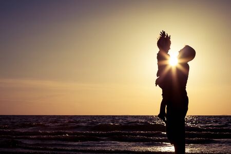 Father and son playing on the beach at the sunset time. People having fun outdoors. Concept of happy friendly family.の写真素材