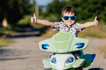 Happy little boy playing on road at the day time. He driving on quad bike in the park. Child having fun on the nature. Concept of happiness.の写真素材