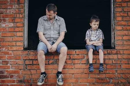 Portrait of young sad little boy and father sitting outdoors at the day time. Concept of sorrow.の写真素材