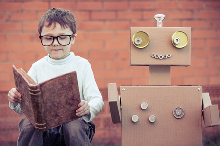 Kid reading next to a robot made of cardboards.の写真素材