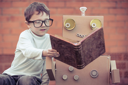 Boy reading to a robot made of cardboard boxes.の写真素材