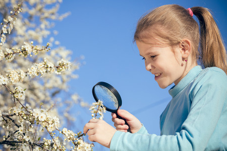 Happy girl studying flowers through a magnifying glass.の写真素材
