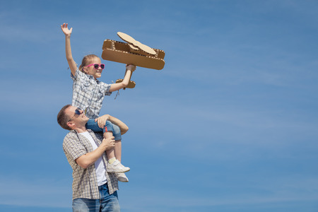 Father and daughter playing with cardboard toy airplane in the park at the day time. Concept of friendly family. People having fun outdoors. Picture made on the background of blue sky.の写真素材