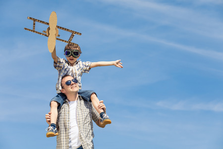 Father and son playing with cardboard toy airplane in the park at the day time. Concept of friendly family. People having fun outdoors. Picture made on the background of blue sky.の写真素材