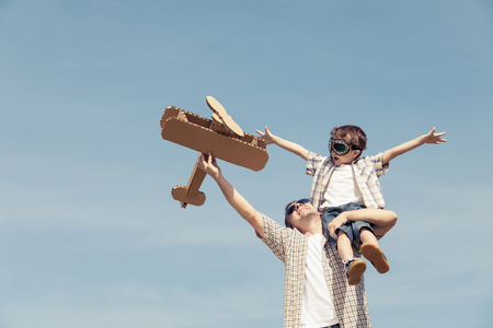 Father and son playing with cardboard toy airplane in the park at the day time. Concept of friendly family. People having fun outdoors. Picture made on the background of blue sky.の写真素材