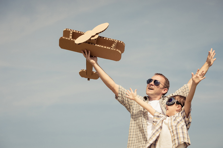 Father and son playing with cardboard toy airplane in the park at the day time. Concept of friendly family. People having fun outdoors. Picture made on the background of blue sky.の写真素材