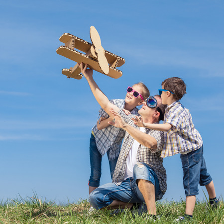 Father and children playing with cardboard toy airplane in the park at the day time. Concept of friendly family. People having fun outdoors. Picture made on the background of blue sky.の写真素材