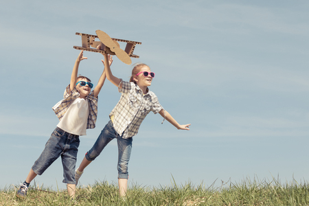 Two little kids playing with cardboard toy airplane in the park at the day time. Concept of happy game. Child having fun outdoors. Picture made on the background of blue sky.の写真素材