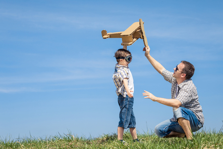 Father and son playing with cardboard toy airplane in the park at the day time. Concept of friendly family. People having fun outdoors. Picture made on the background of blue sky.の写真素材