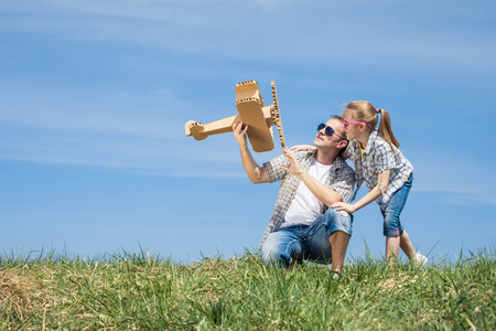 Father and daughter playing with cardboard toy airplane in the park at the day time. Concept of friendly family. People having fun outdoors. Picture made on the background of blue sky.の写真素材