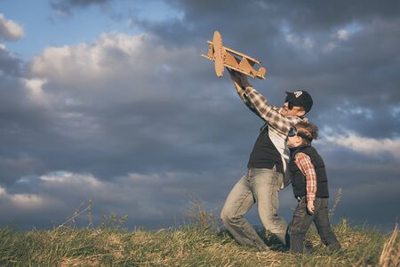 Father and son playing with cardboard toy airplane in the park at the day time. Concept of friendly...
