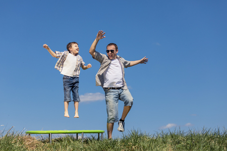 Father and son playing on the field at the day time. People having fun outdoors. They jumping on trampoline on the lawn. Concept of friendly family.の写真素材